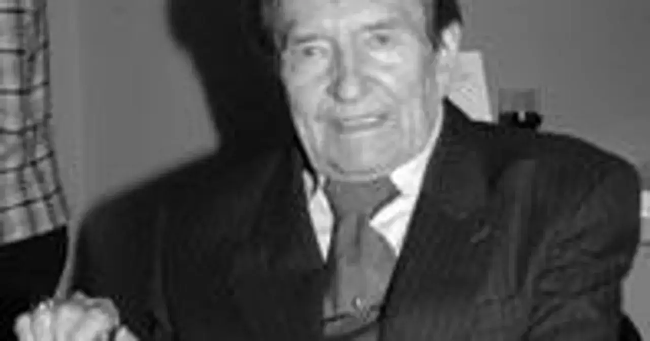 Portret Wieńczysława Glińskiego, uśmiechniętego, w garniturze i krawacie. W tle widać fragment kraty.