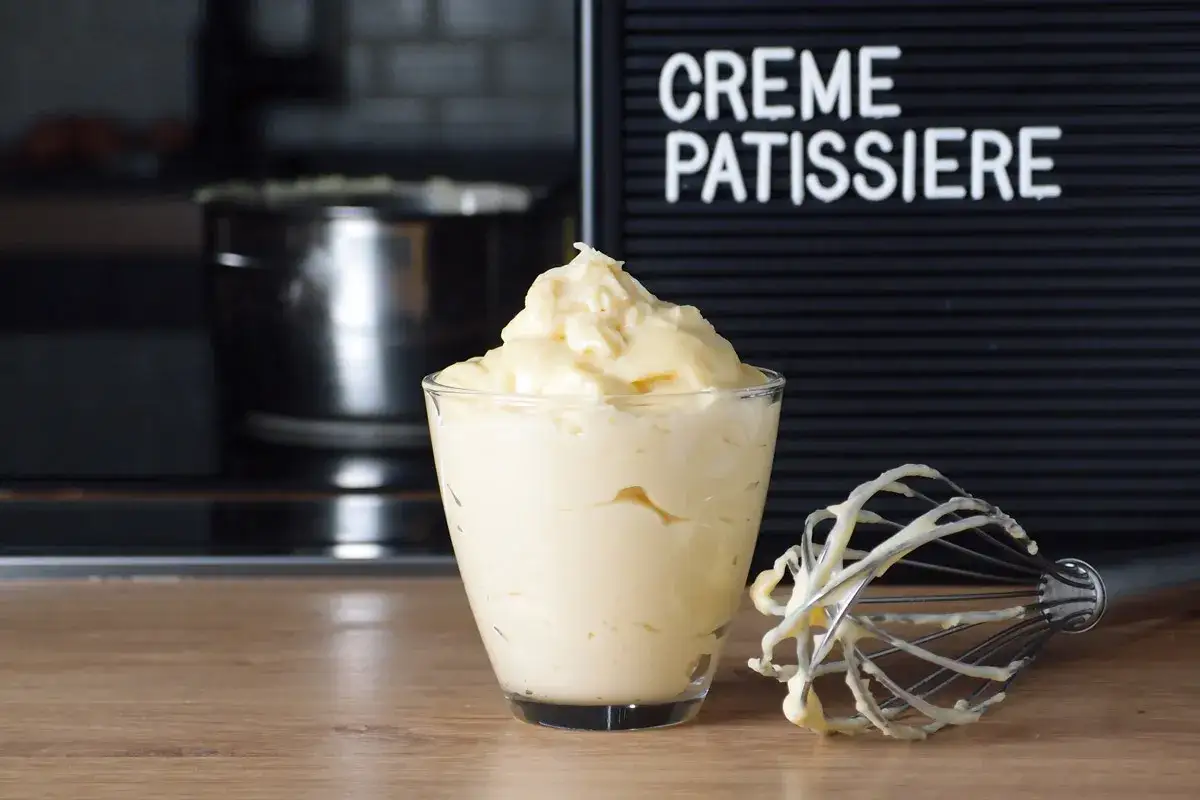 Verre rempli de cr&egrave;me p&acirc;tissi&egrave;re onctueuse, avec un fouet couvert de cette d&eacute;licieuse pr&eacute;paration &agrave; c&ocirc;t&eacute;. Le mot 