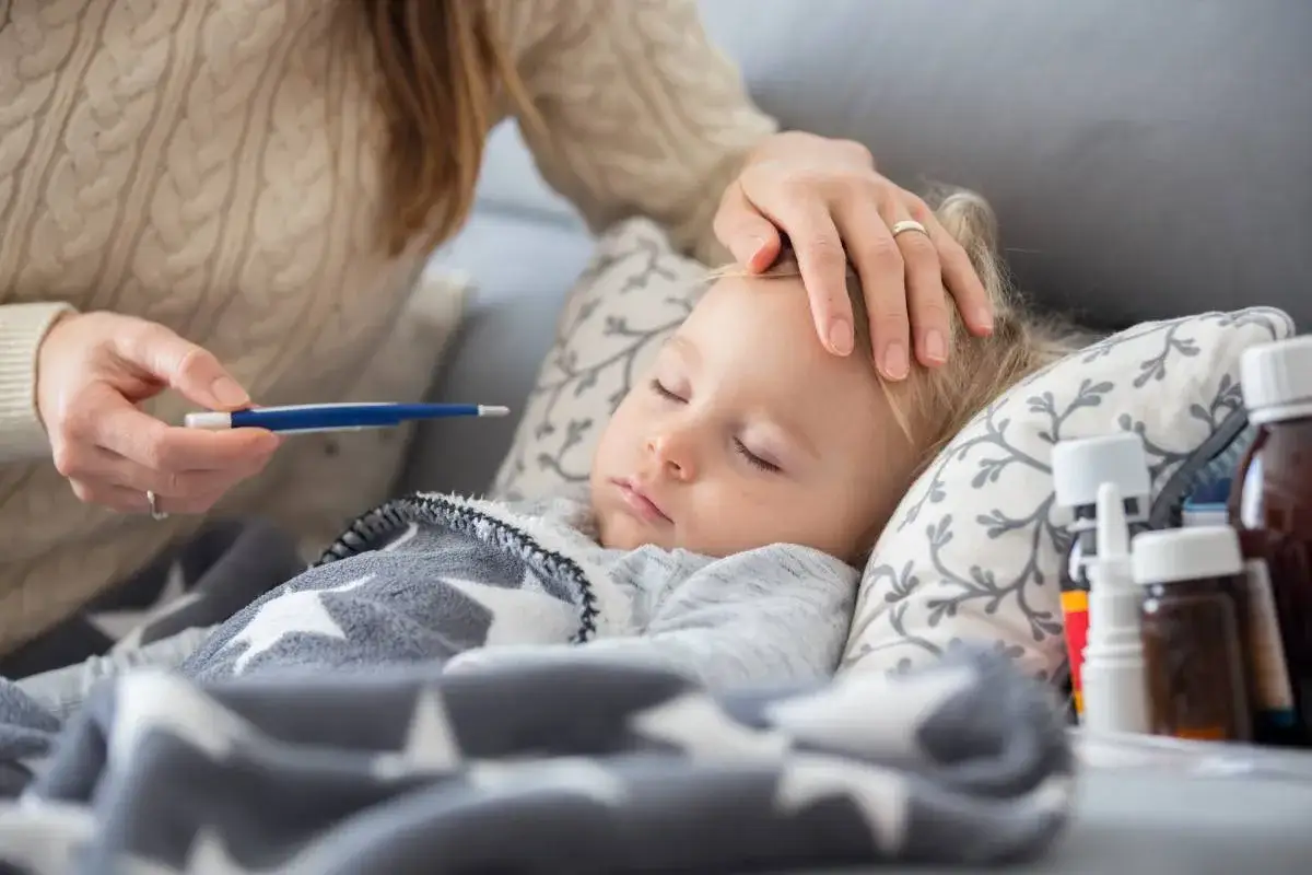 Mama mierzy gorączkę choremu dziecku, które śpi pod gwiazdkowym kocem. Kolejne choroby w przedszkolu to smutna rzeczywistość.