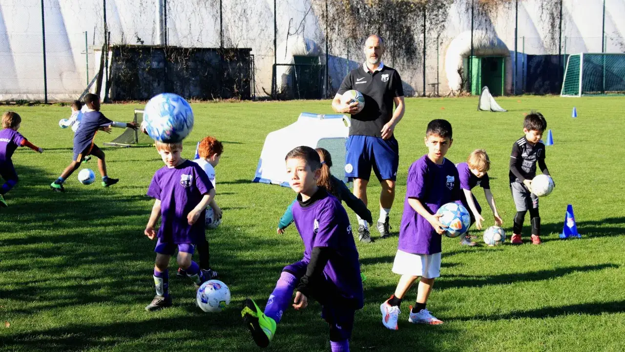 Kinder trainieren Fu&szlig;ball in Berlin. Ein Trainer beobachtet die jungen Spieler auf dem Rasen.