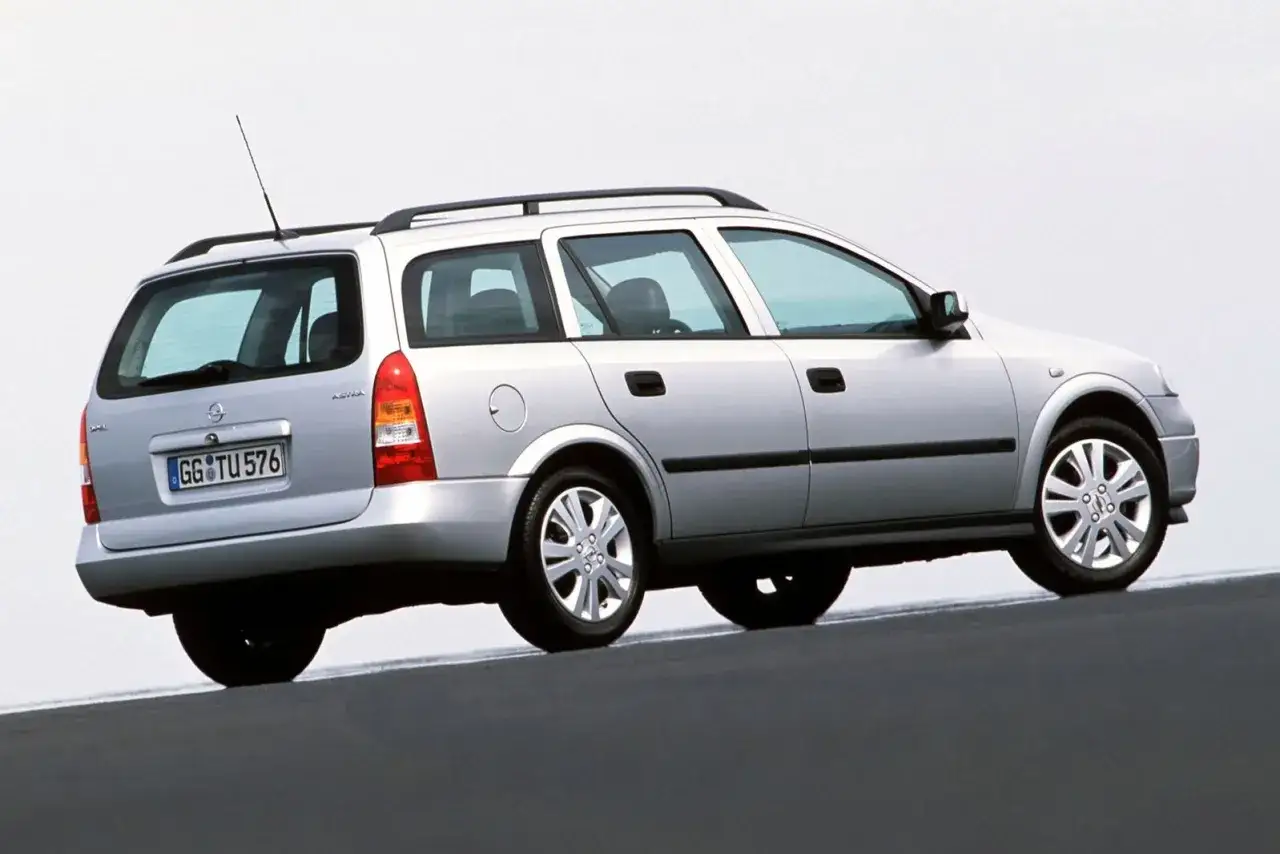 Srebrny Opel Astra G CC kombi z relingami dachowymi, widok z tyłu i boku, na tle jasnego nieba.