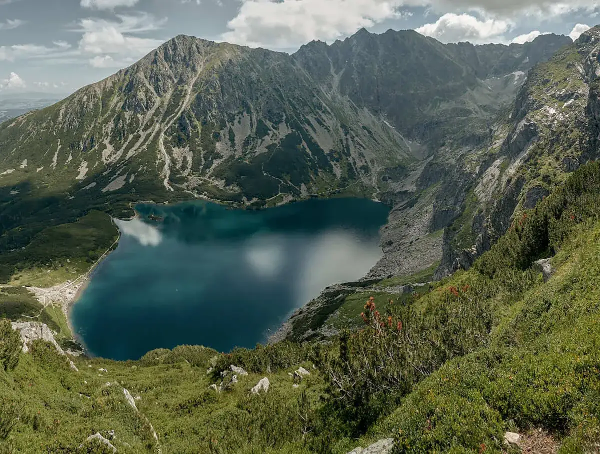 Widok na turkusowe jezioro i skaliste szczyty. Szlak na Kościelec prowadzi przez zielone zbocza.