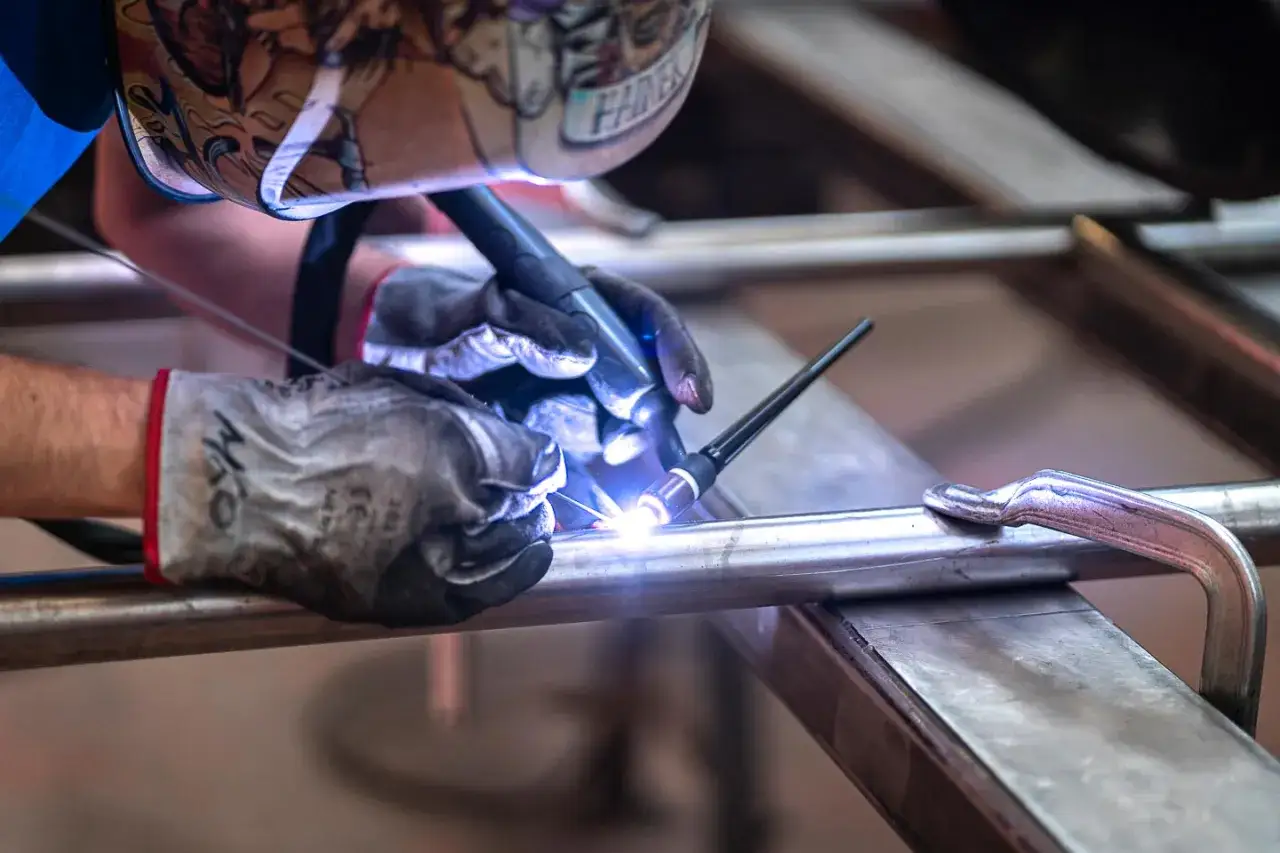 Un saldatore con maschera decorata unisce tubi metallici, mostrando il vero significato del welding: creare legami resistenti.