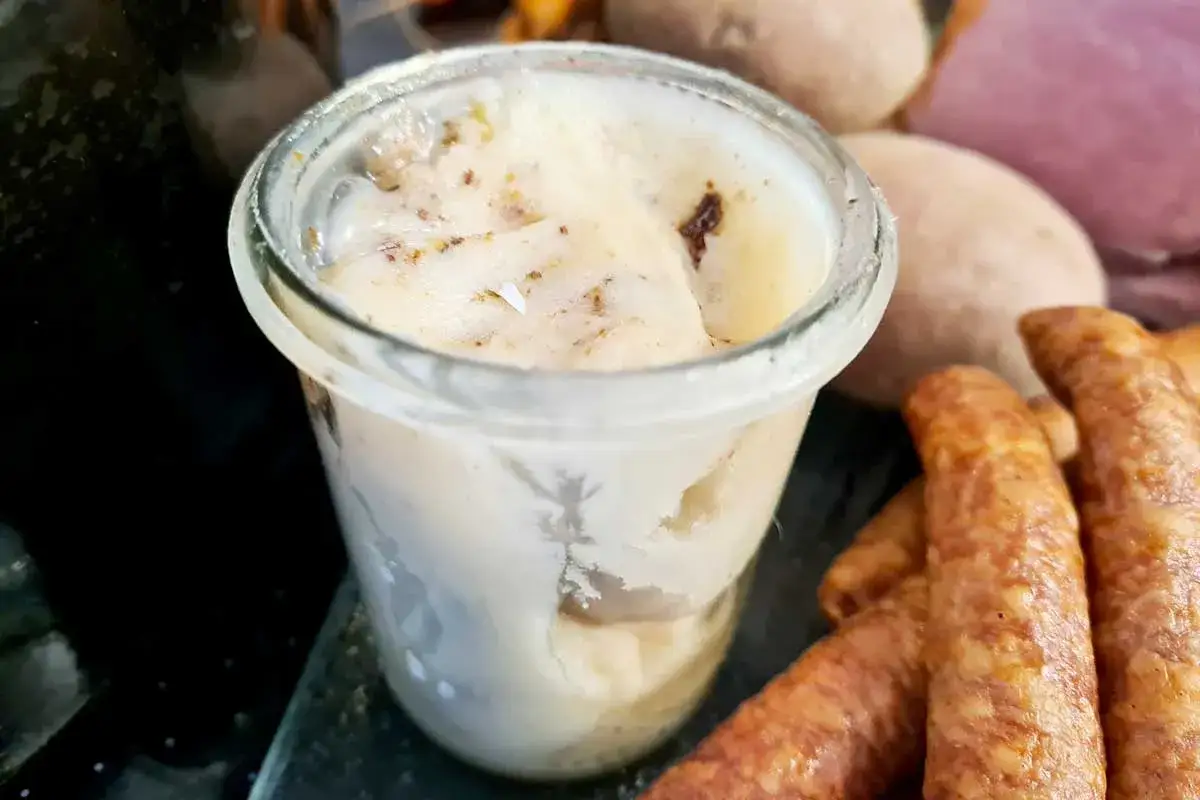 Frisch zubereitetes Schmalz im Glas, bereit zum Genießen. Daneben liegen Bratwürste und Kartoffeln.