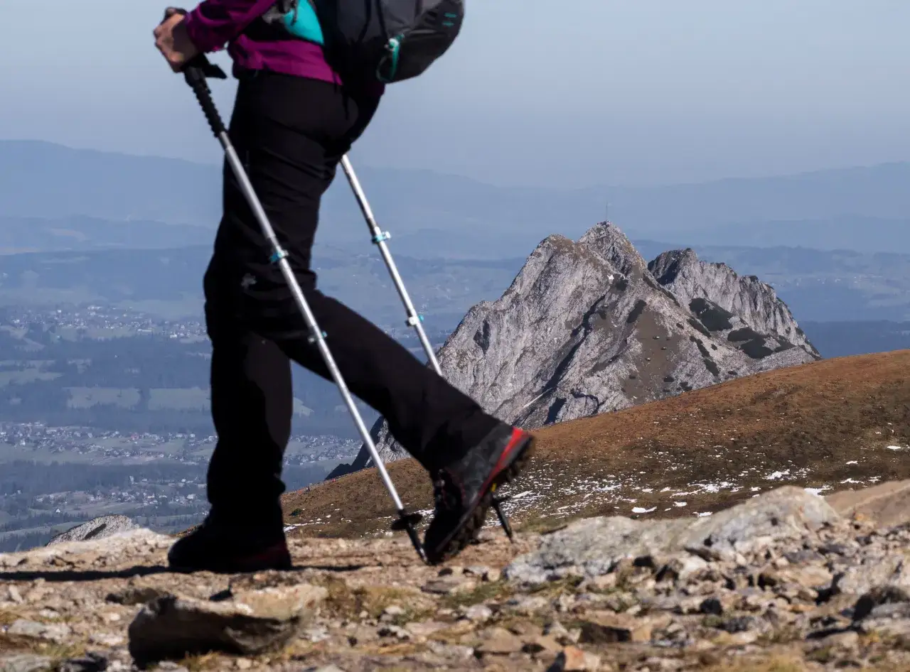 Osoba z kijkami trekkingowymi o złej wysokości na trasie, z widokiem na góry i dolinę.