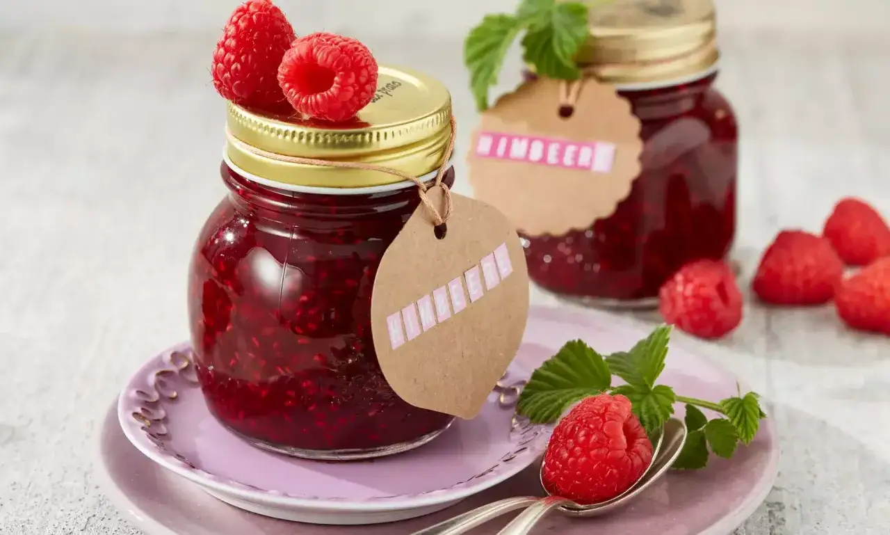 Selbstgemachte Himbeermarmelade im Glas, garniert mit frischen Fr&uuml;chten. Ein k&ouml;stliches Rezept f&uuml;r den Sommer.