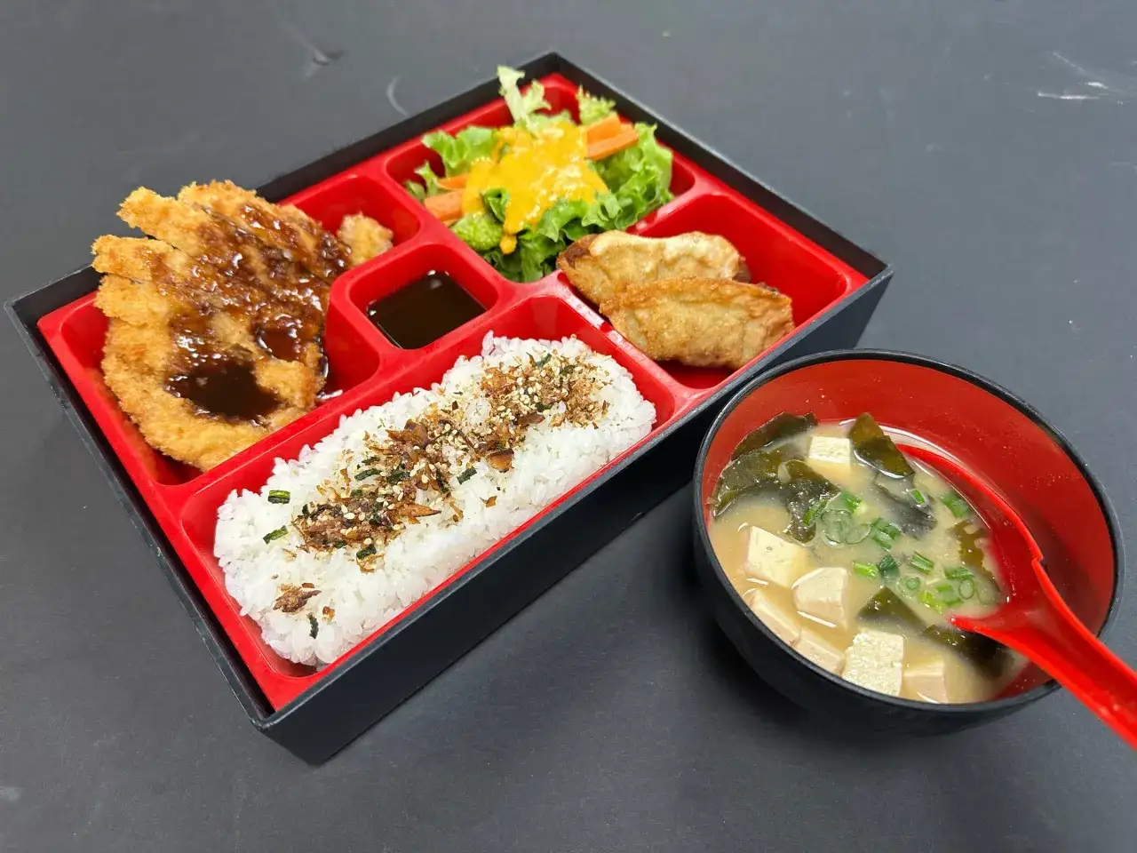 A delicious pork katsu bento box with rice, salad, gyoza, and miso soup.