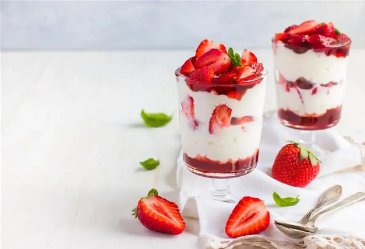 Deux verrines fraise fromage blanc, garnies de fruits frais et de feuilles de menthe, sur un fond blanc.