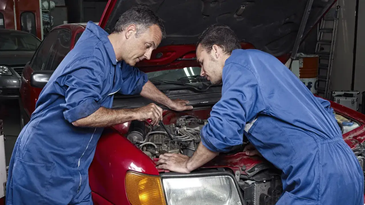 Dos mec&aacute;nicos trabajan en el motor de un coche rojo. Demuestran que merece la pena arreglar un coche de 20 a&ntilde;os.