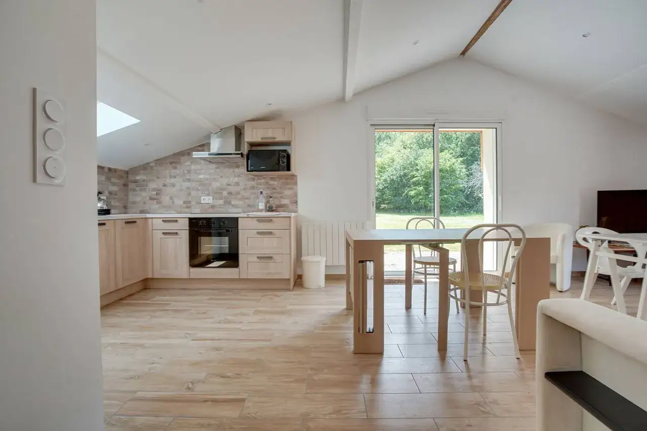 Cuisine moderne dans une ancienne grange transformée en habitation. Parquet clair, murs en briques apparentes, grande baie vitrée donnant sur la verdure.