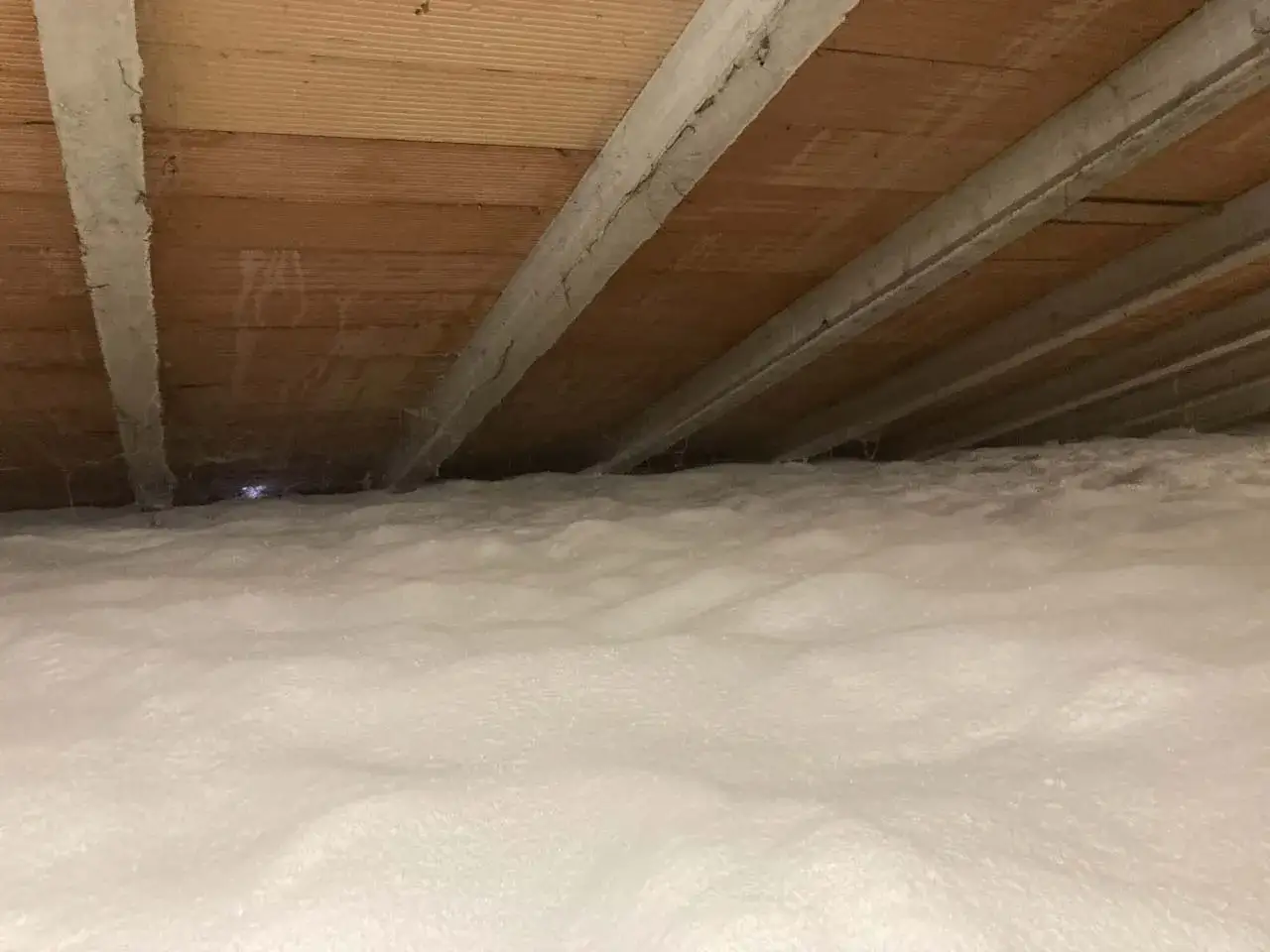 Spessore isolamento sottotetto non abitabile con schiuma espansa. Il soffitto in legno &egrave; visibile sopra la soffice coltre bianca.