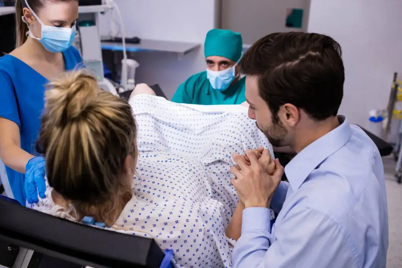 Padre apoya a madre en trabajo de parto, mientras enfermera y doctor observan. Un momento crucial para como provocar el parto.