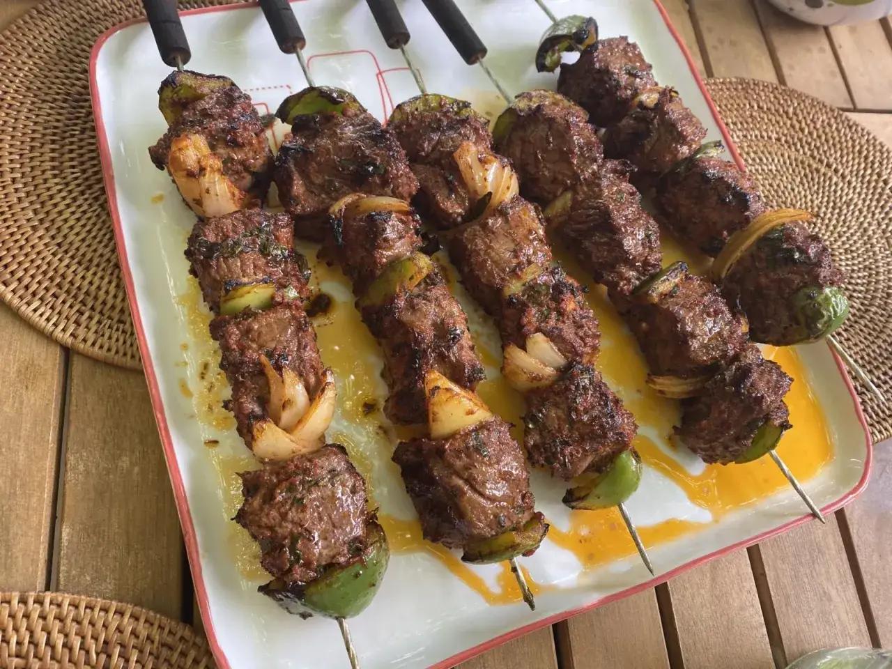 Brochettes de b&oelig;uf marin&eacute;es, grill&eacute;es &agrave; la perfection avec des oignons et des poivrons verts, servies sur un plat blanc.