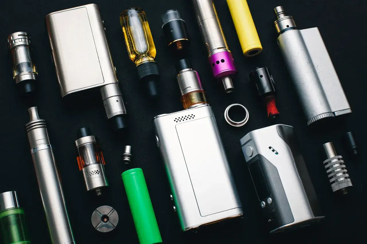 Vap que es: varios dispositivos de vapeo, baterías y líquidos en fondo negro.