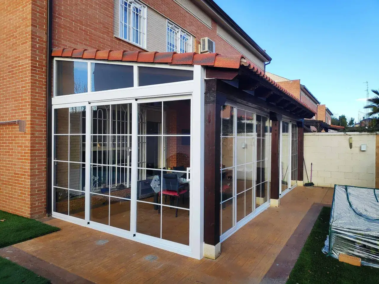 Moderno cierre para balcones y terrazas con grandes ventanales blancos y estructura de madera oscura.