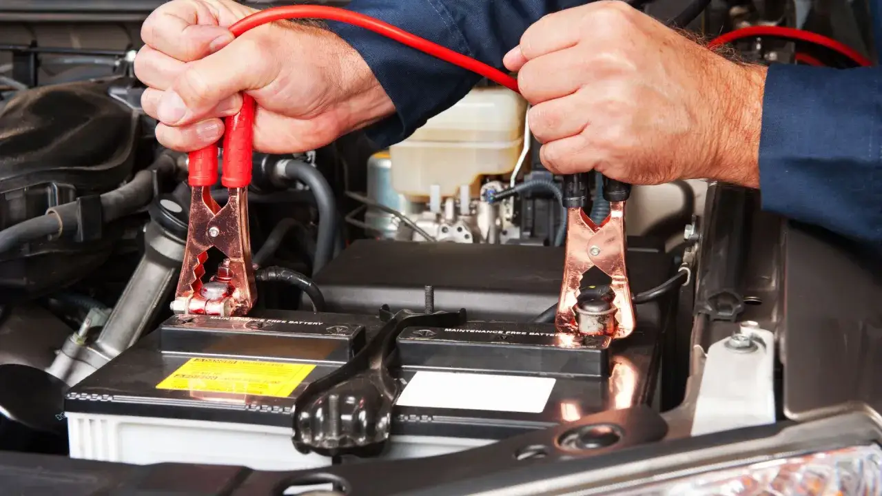 Mani che collegano i cavi alla batteria dell'auto, un passaggio fondamentale per capire come montare una batteria o per avviarla.