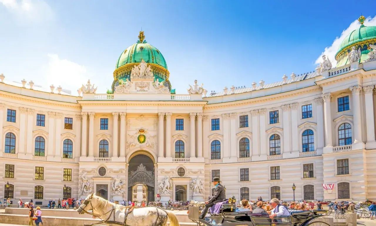 Hofburg zwiedzanie: pow&oacute;z konny przed pałacem z zieloną kopułą. Turyści spacerują po placu.