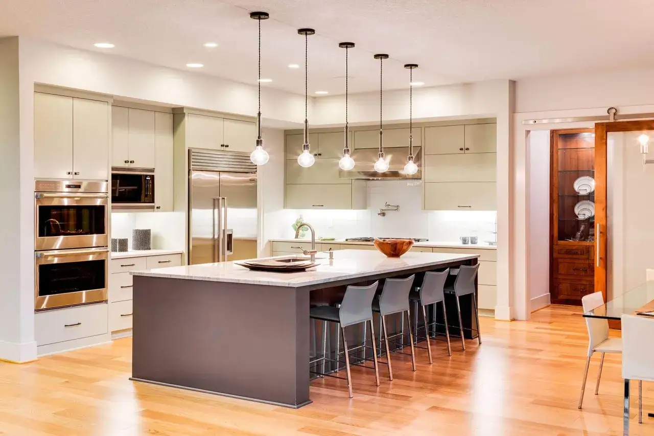 Cocina moderna con isla central, taburetes y una lámpara colgante que ilumina el espacio.