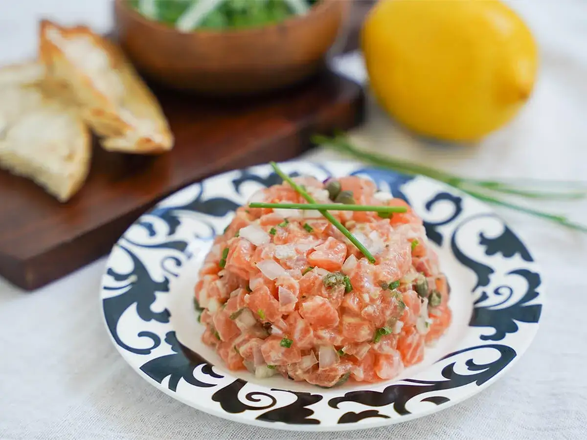 Delicioso tartar de salmón fresco, picado finamente con cebolla y alcaparras, servido en un plato decorado.