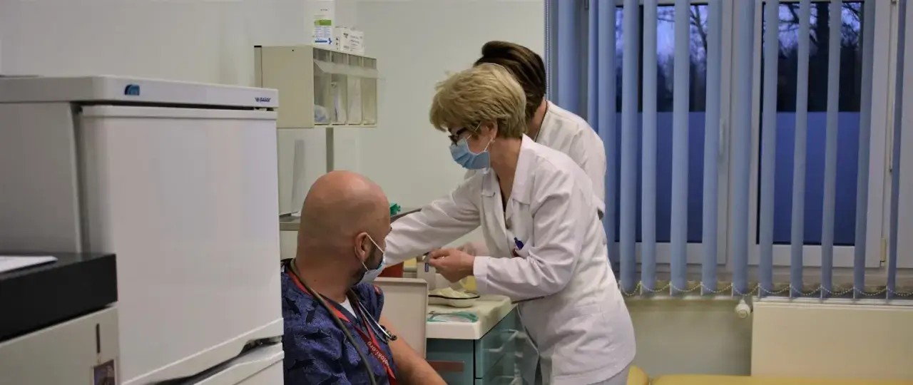 Pielęgniarka podaje szczepienia covid. Pacjent siedzi, pielęgniarka przygotowuje zastrzyk.