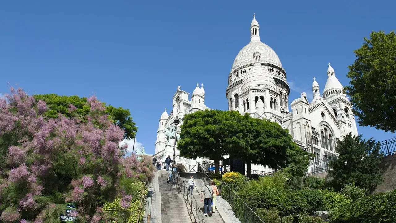 Treppen f&uuml;hren zur Sacr&eacute;-C&oelig;ur-Basilika im Montmartre Viertel. Bl&uuml;hende B&auml;ume s&auml;umen den Weg.