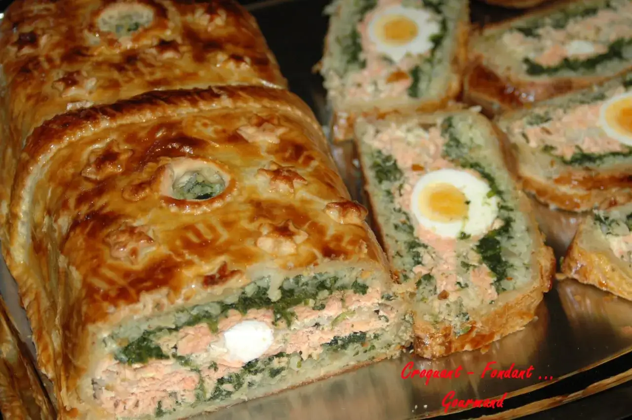 Un koulibiac de saumon doré, garni d'épinards et d'œufs durs, est coupé en tranches généreuses.