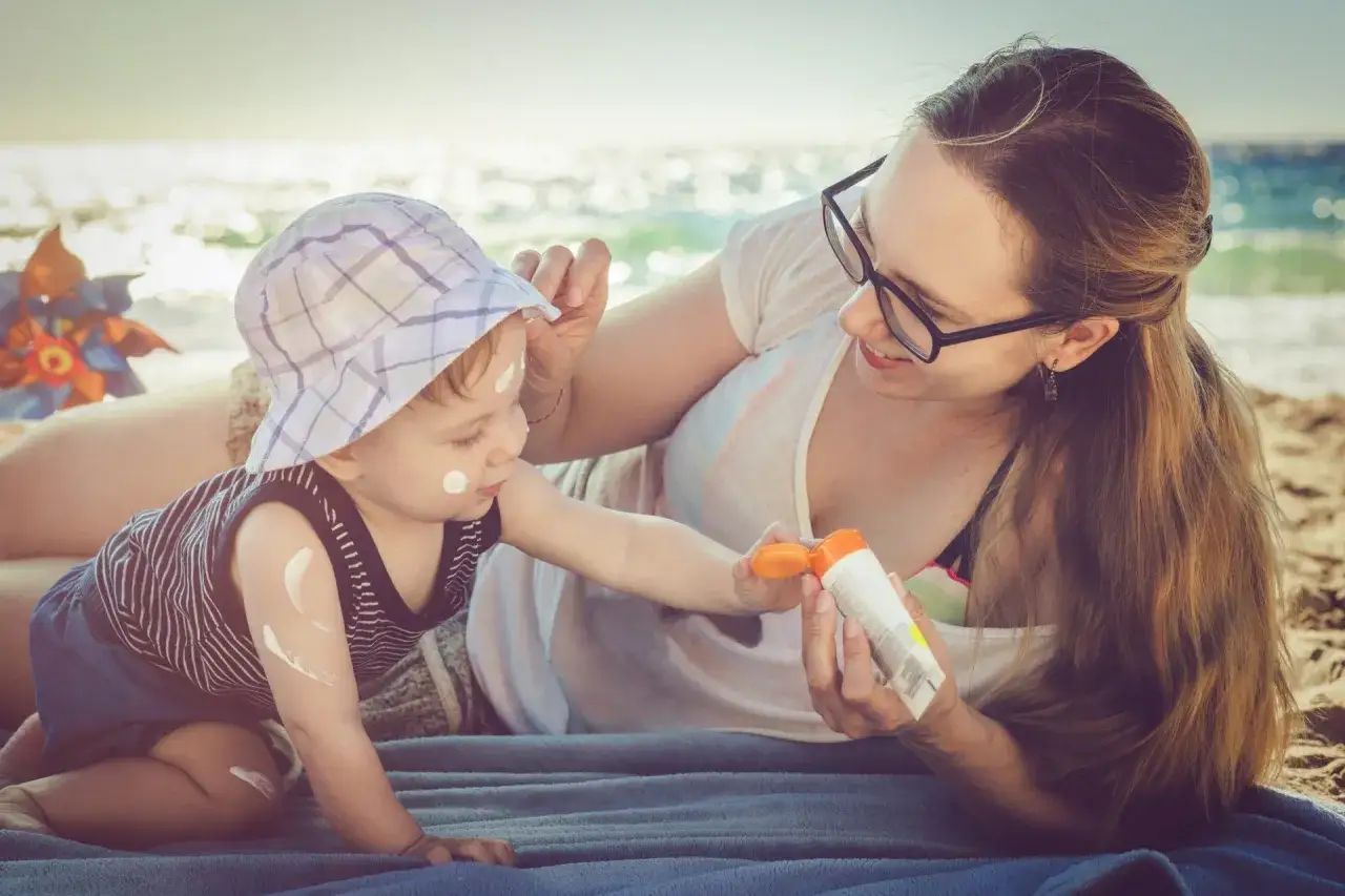 Mama smaruje dziecko kremem na plaży, chroniąc je przed oparzeniami słonecznymi.