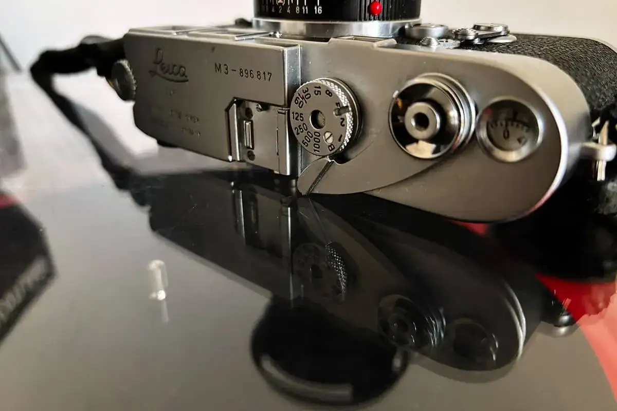 Close-up of a vintage Leica M3 camera, showing its silver body, film speed dial, and strap lug.