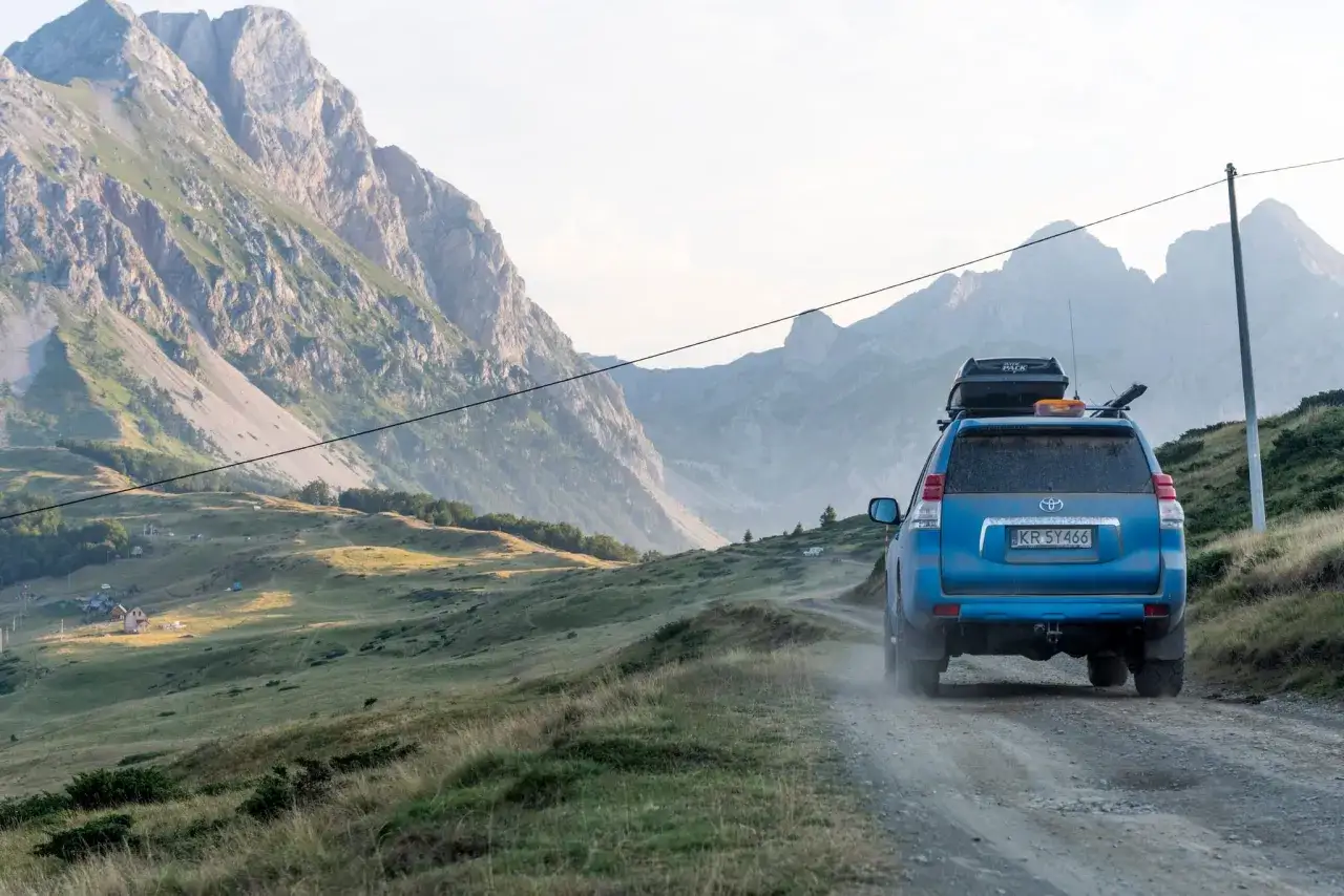Niebieski SUV jedzie po szutrowej drodze w górach Czarnogóry. Uważaj na wyboje i strome podjazdy, podróżując po takich terenach.