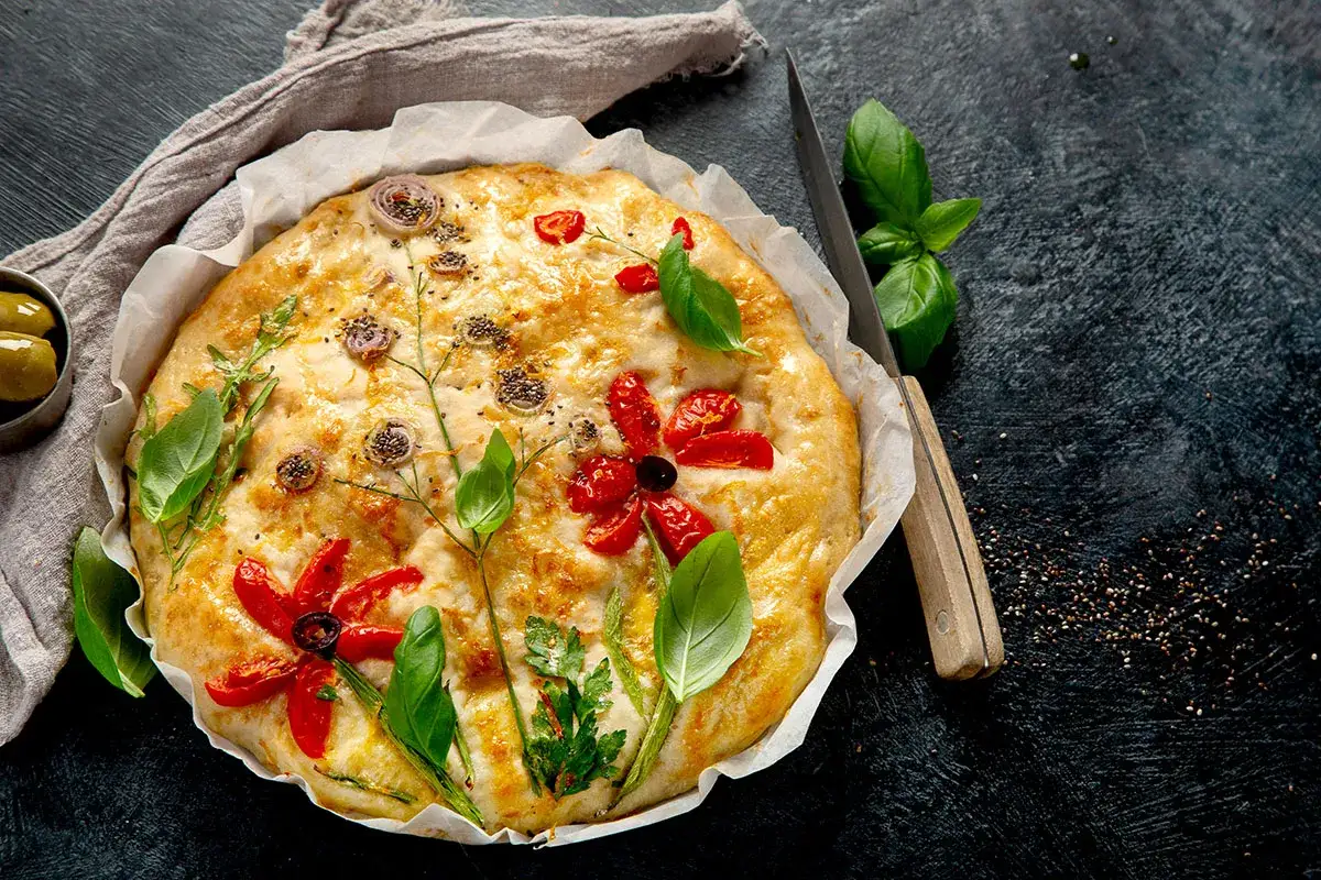 Kreativ belegte Focaccia mit Tomatenblumen und Kr&auml;utern, die wie ein Garten aussieht.