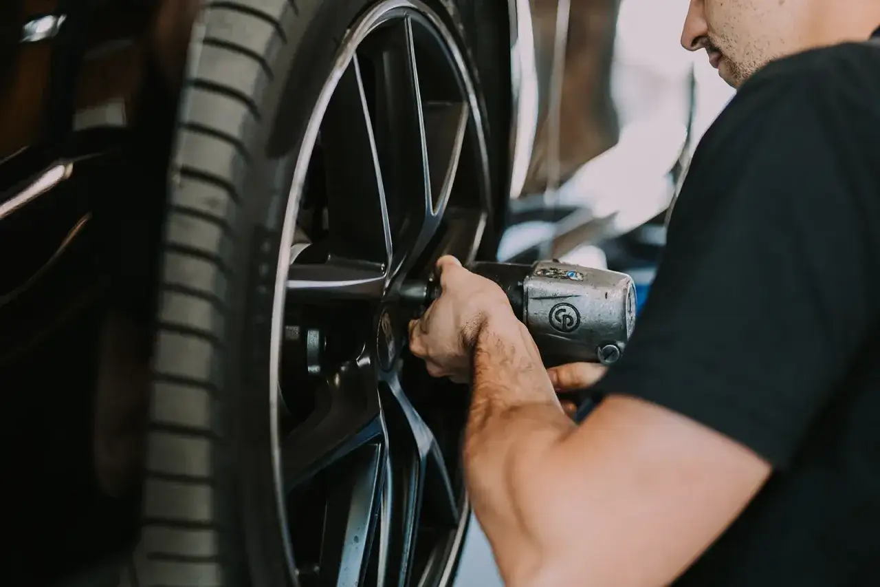 Mechanik dokręca śruby w feldze, przygotowując auto do sezonu. Czas pomyśleć, kiedy wymienić opony na letnie.