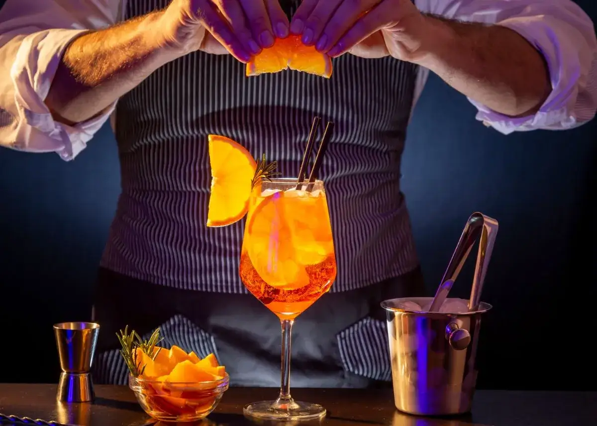 Un barman decora un Aperol Spritz, evocando su origen italiano. Naranja, hielo y romero realzan el vibrante color.
