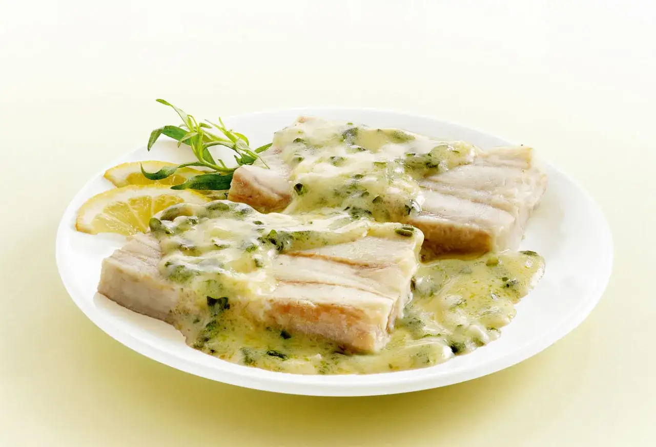 Deux pavés de poisson nappés d'une onctueuse sauce à l'oseille, accompagnés de quartiers de citron et d'une herbe fraîche.