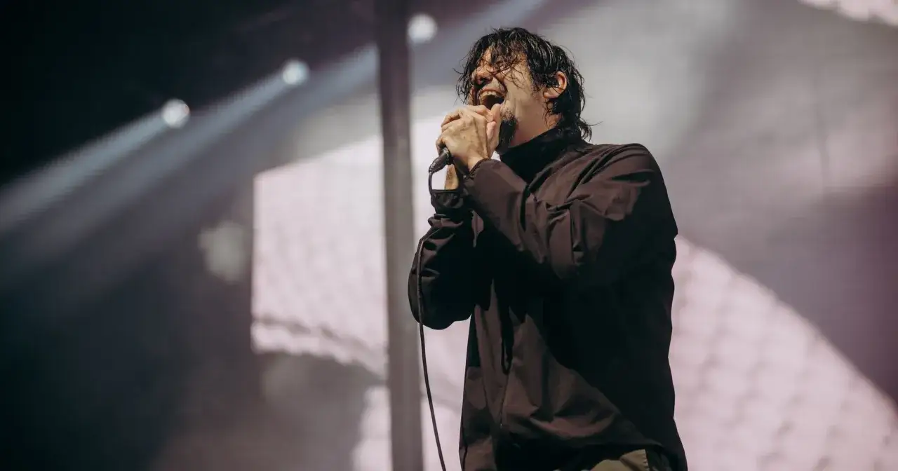 Chino Moreno z Deftones na koncercie w Polsce, z mikrofonem w dłoniach, w emocjonalnym geście.