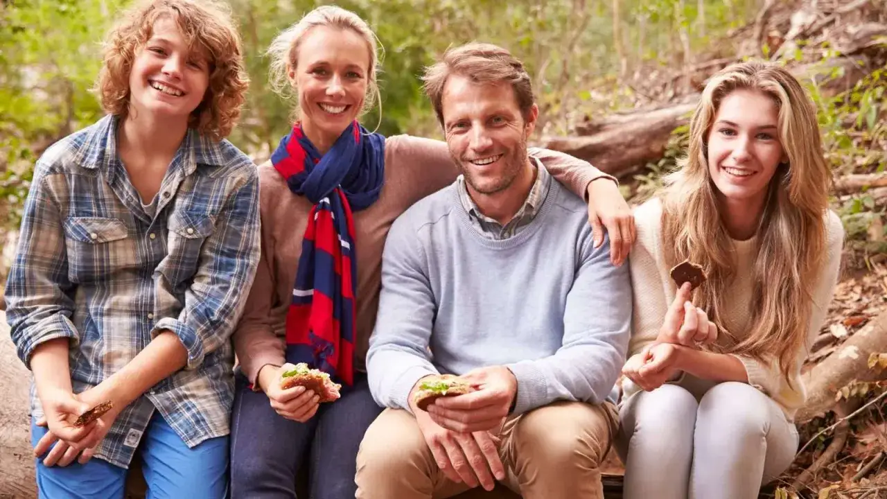 Famiglia felice in vacanza con ragazzi di 15 anni, seduti all'aperto con panini e biscotti.