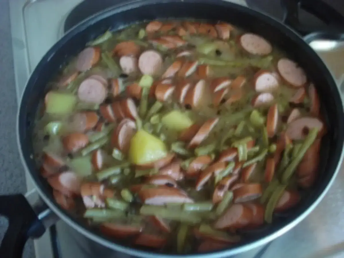 Ein deftiges schnippelbohnen rezept mit Kartoffeln und W&uuml;rstchen in einem Topf.