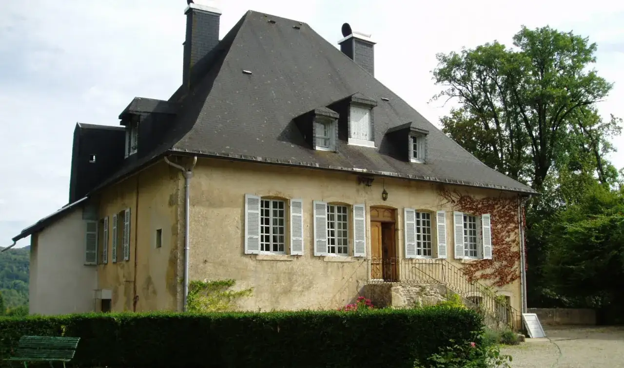 Maison de campagne avec un toit en ardoise, des volets blancs et une partie de la tour de Saint Lupicin.