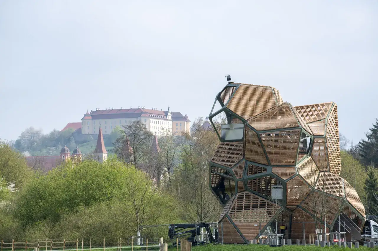 Ein futuristisches Holzgeb&auml;ude steht vor einer historischen Schlossanlage. Die Bundesgartenschau ist ein Ereignis, das man sich nicht entgehen lassen sollte.