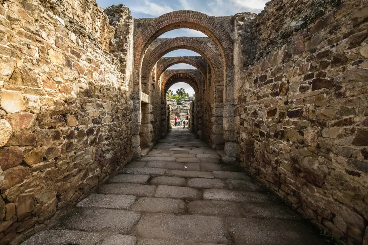 Antiguos arcos de ladrillo y piedra a lo largo de la Vía de la Plata, con un camino empedrado y turistas al fondo.