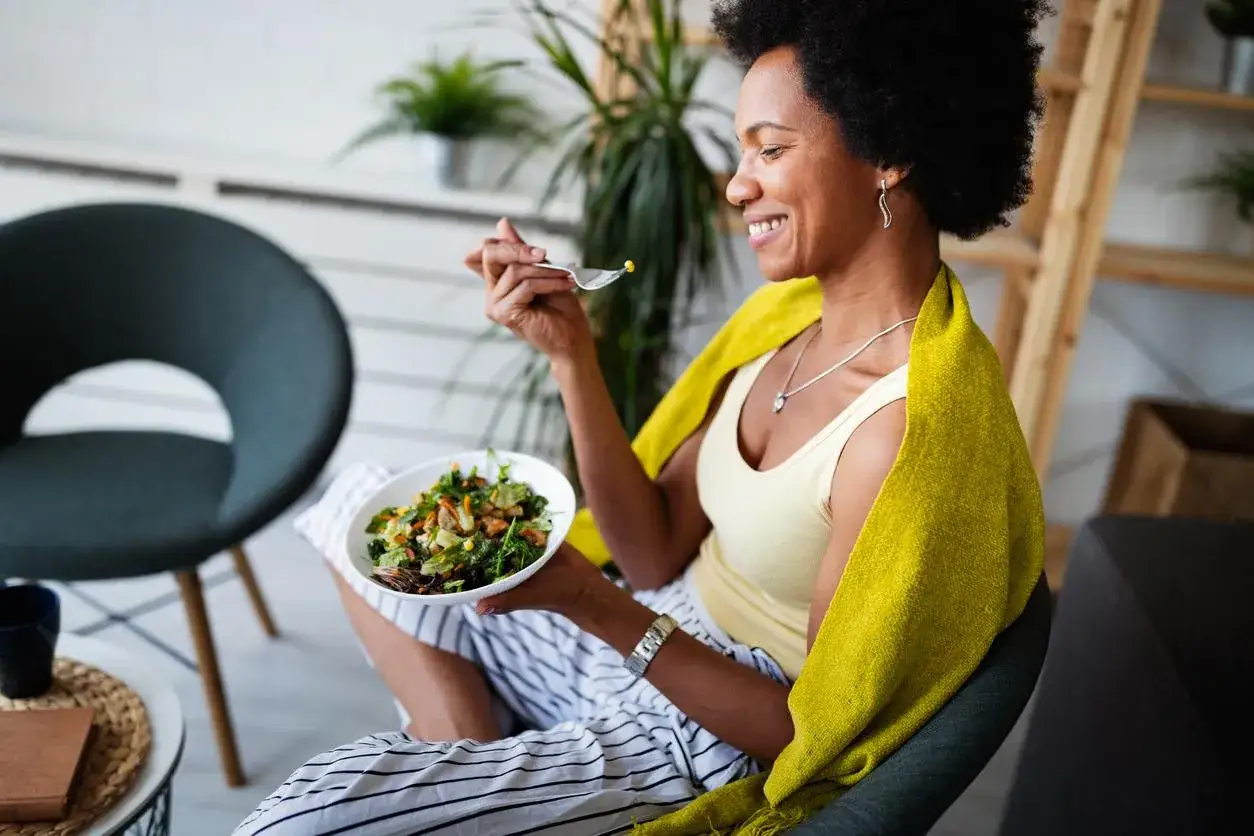 Femme souriante mangeant une salade, profitant d'un repas sain pour &eacute;viter la prise de poids.