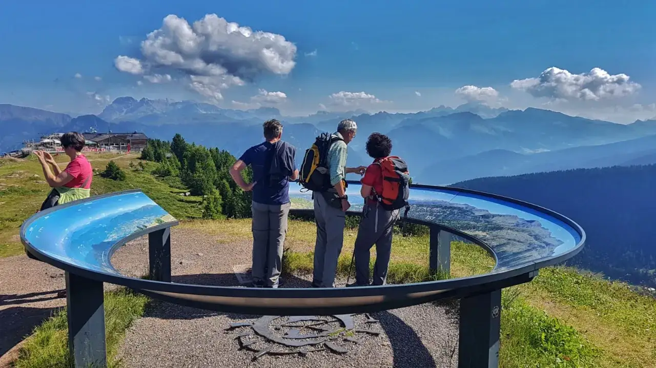 Tre escursionisti ammirano il panorama mozzafiato dei laghi di Bombasel, indicando la mappa panoramica.
