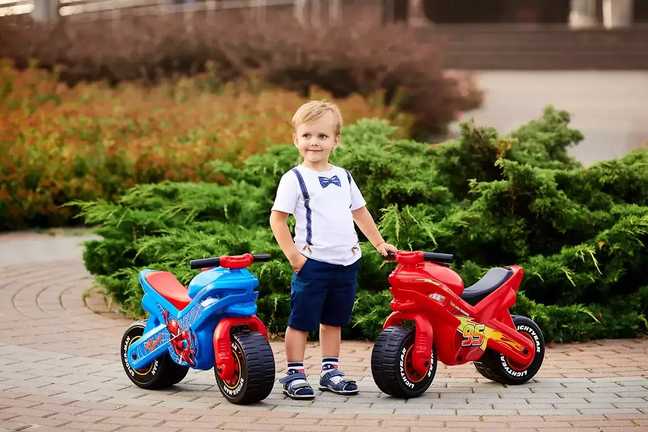 Chłopiec w ogrodzie z dwoma motorkami. Idealny ranking zabawek dla 2-latka chłopca: czerwony Zygzak McQueen i niebieski Spider-Man.