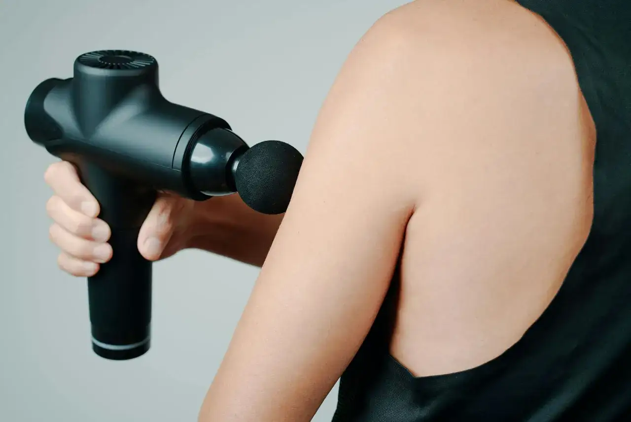 En hand håller en svart massagepistol mot en arm. Kan vara användbar för massage under graviditet.