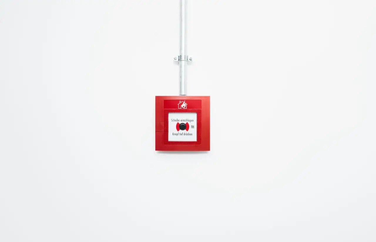 Roter Feuermelder an wei&szlig;er Wand, wie in der Landesbauordnung Bremen vorgeschrieben. 