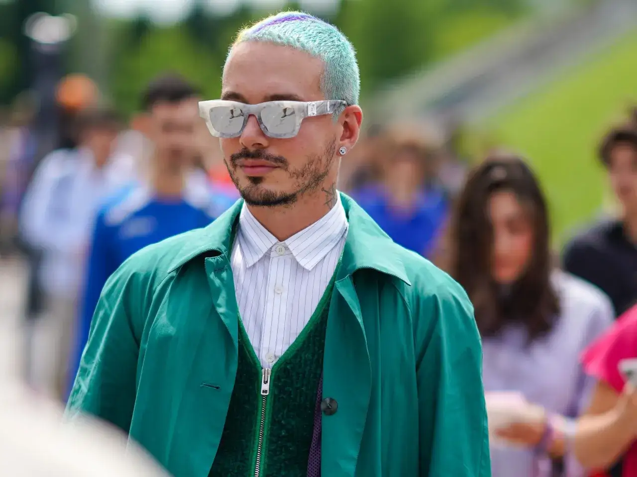 Hombre con cabello teñido de azul verdoso y morado, gafas llamativas y un look moderno que explora diversos tipos de buzz cut.