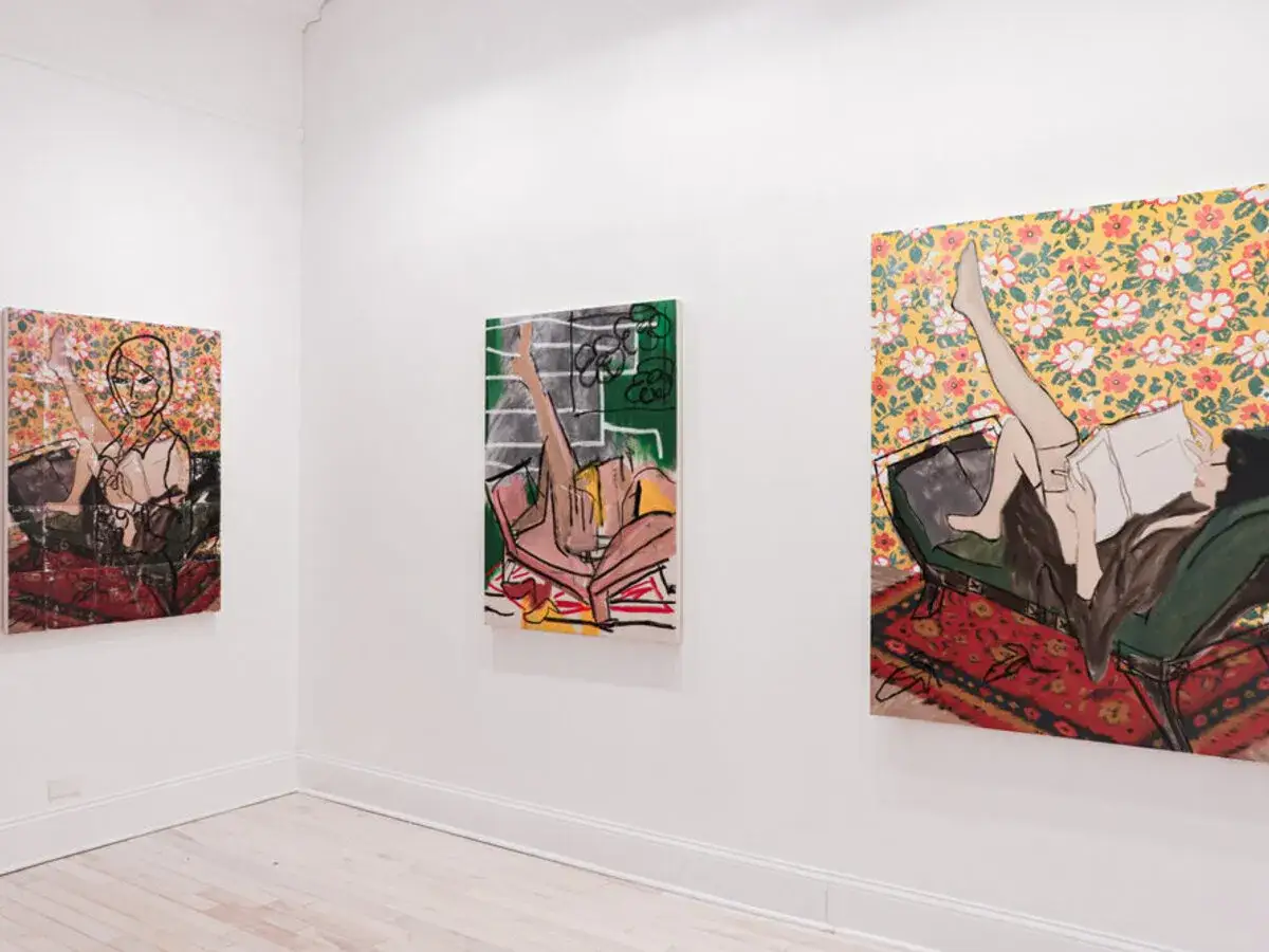 Three vibrant paintings by Lucy Liu hang on a white gallery wall, depicting stylized figures in relaxed poses.