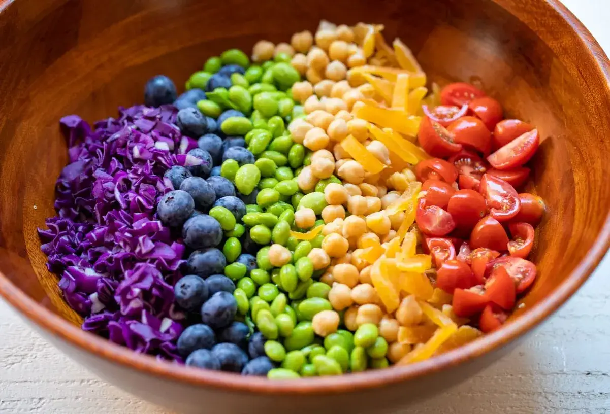 Bunter gemischter Salat in einer Holzschale: Rotkohl, Blaubeeren, Edamame, Kichererbsen, gelbe Paprika und Kirschtomaten.