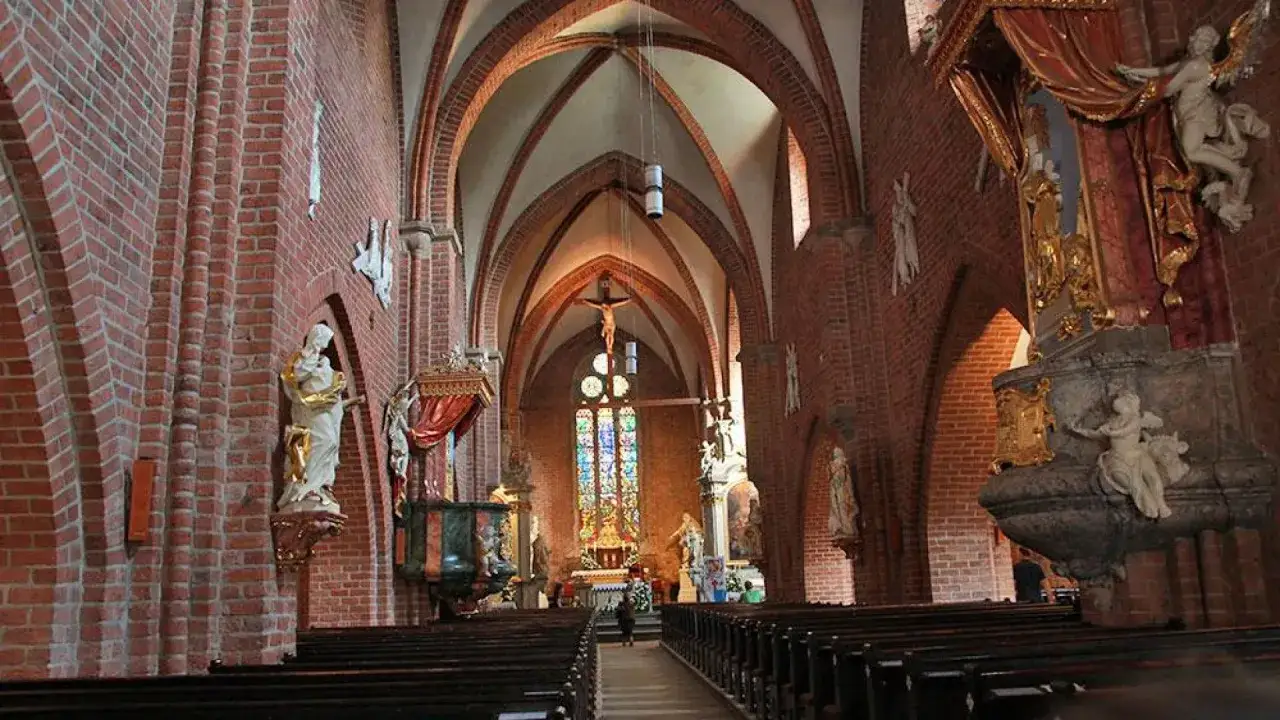 Wnętrze opactwa cystersów w Rudach. Gotyckie sklepienie, ceglane ściany, ołtarz z witrażem i krucyfiks.