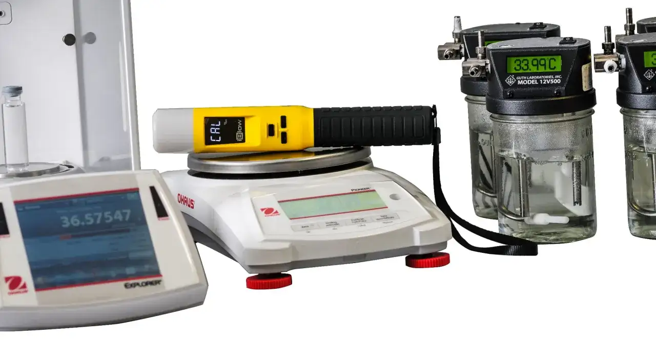 Xblitz Spirit kalibracja. Ż&oacute;łty tester na wadze Ohaus Pioneer. Obok wagi laboratoryjne i cylindry z płynem.