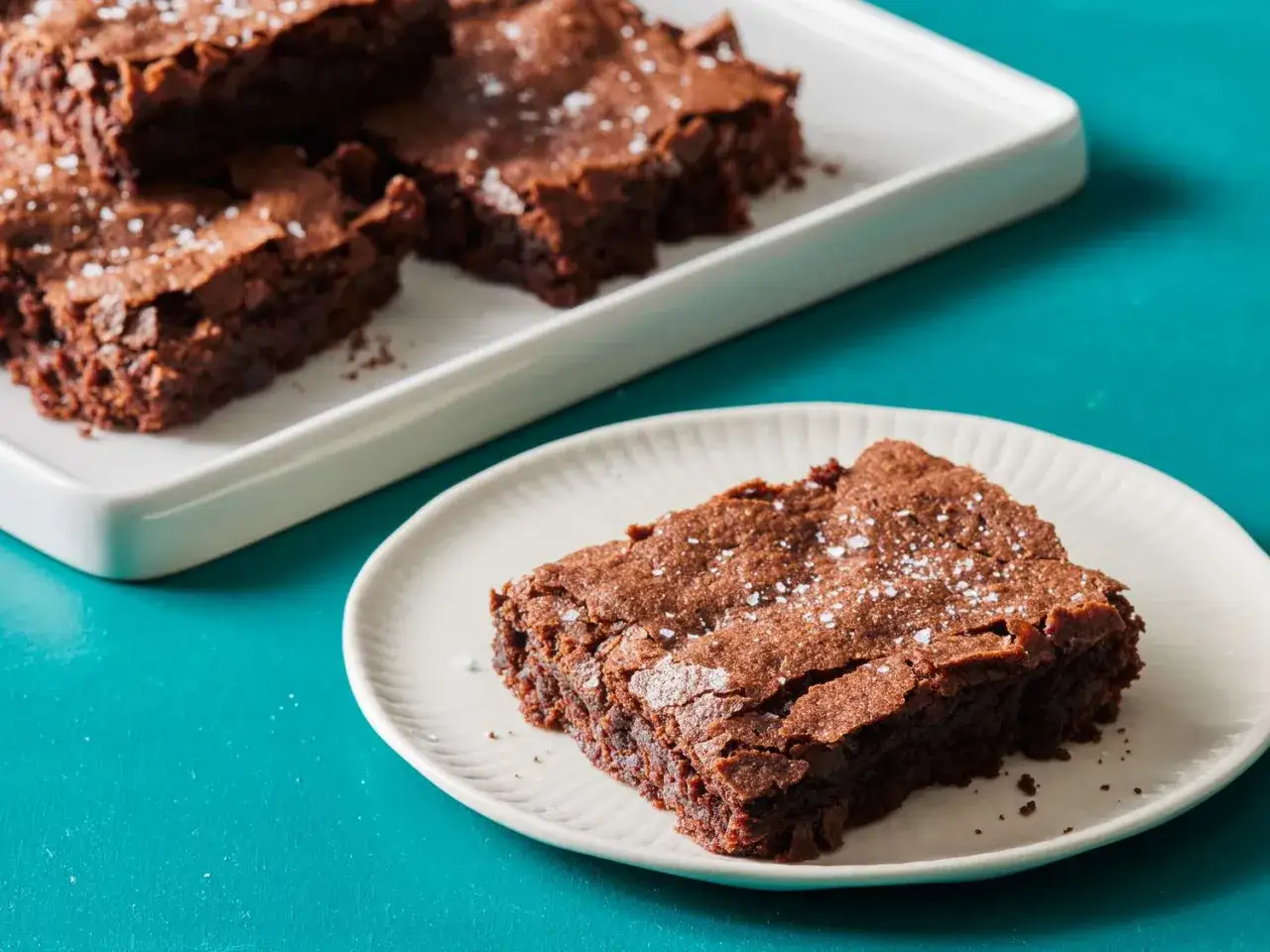 Saftige Brownies, perfekt für jedes Brownie Rezept, mit Meersalz bestreut. Ein Stück auf einem Teller, der Rest auf einer weißen Platte.